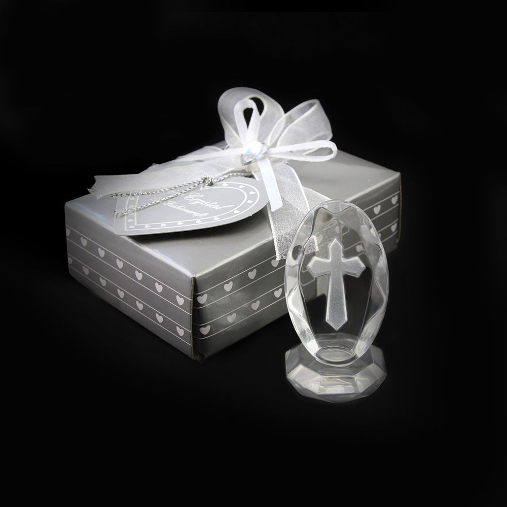 Crystal cross ornament in front of a gift box with a white ribbon on a black background