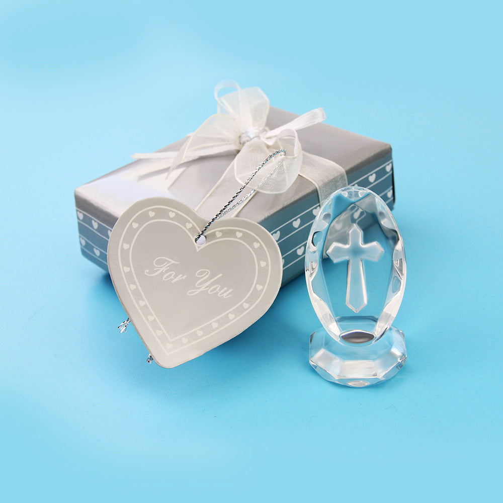 Crystal cross ornament next to a gift box with a heart-shaped tag on a blue background