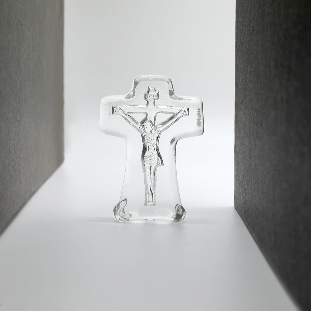 Clear glass crucifix on a white surface with gray background